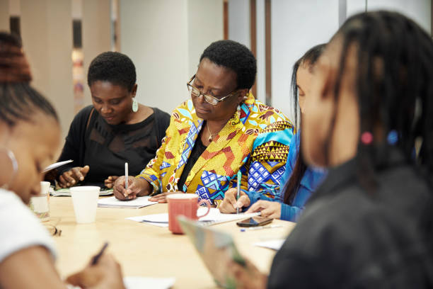 istockphoto-1055419270-612×612 Shot of a group of confident women writing on paper while being seated at a table during a meeting inside a community centre